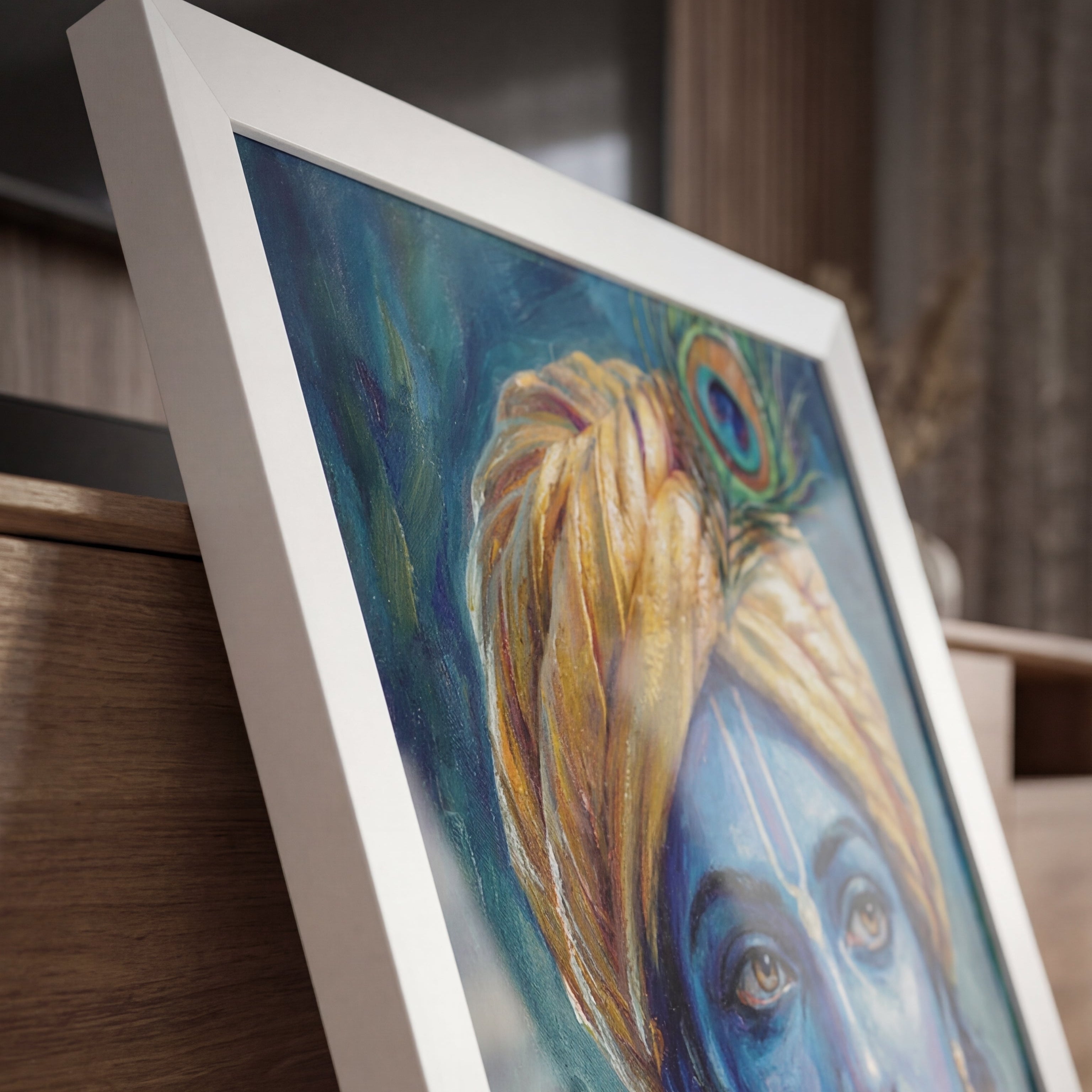 Framed painting of a blue-skinned figure with a peacock feather on a wooden surface.